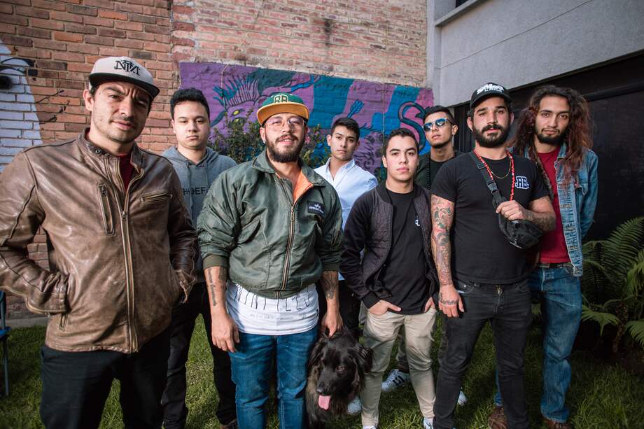 Foto de los ocho integrantes de Radio Bembé en un patio con mural, publicada por El Espectador